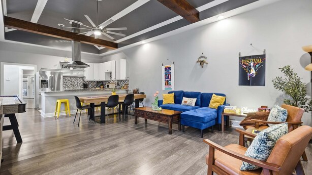 Uma sala ampla com sofá azul, mesa de centro de madeira e um espaço de refeições com cadeiras e um banquinho amarelo.