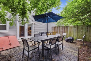 A patio with a table and chairs, a blue umbrella, and a wooden fence.