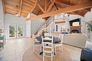 A spacious living area with a high ceiling, a fireplace, a dining table with chairs, and a staircase leading to another level.
