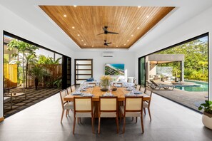 A modern dining area with a wooden ceiling, large windows, and a view of an outdoor pool.