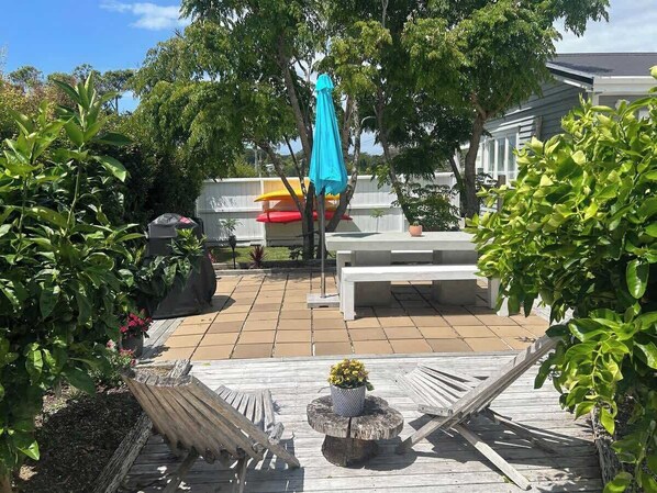 Een terras met een houten dek, een ronde tafel met een plant in pot en een blauwe parasol.