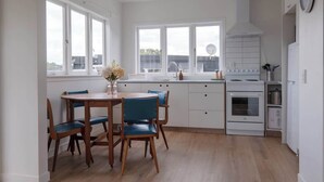 Ett modernt kök med vita skåp, ett matbord med blå stolar och en utsikt genom stora fönster.