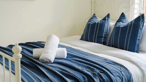 Un lit bien fait, avec une couvre-lit à rayures bleues et des oreillers blancs, une tête de lit blanche et un petit tableau encadré accroché au mur.