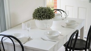 Une table à manger blanche, dressée avec des bols blancs, une plante en pot, des verres à vin et des couverts.