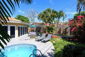 Un jardin avec une piscine, des chaises longues, un espace salon abrité et des plantes tropicales.