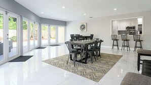 A spacious dining area with a large table and chairs, a kitchen area with modern appliances, and a view of the outdoors through large sliding doors. - Private Pool 4BR · 6 Min to Fort Lauderdale Beach (Fort Lauderdale)