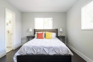 Une chambre à coucher comprenant un lit, deux tables de chevet, une fenêtre et une porte donnant sur une salle de bain.