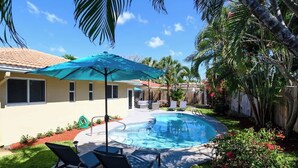 A backyard with a swimming pool, lounge chairs, and a blue umbrella. - Private Pool 4BR · 6 Min to Fort Lauderdale Beach (Fort Lauderdale)