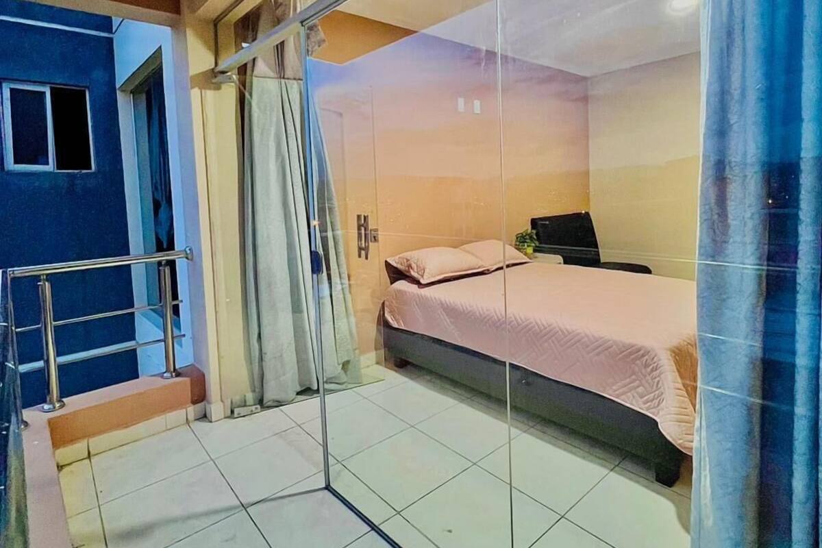 Een slaapkamer met een bed, een bureau en een stoel. Er is een raam met gordijnen, een deur en een trap die naar een verdieping leidt.