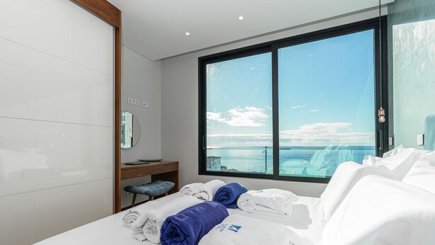 Ett modernt hotellrum med en stor säng, ett skrivbord, en stol och utsikt över havet.