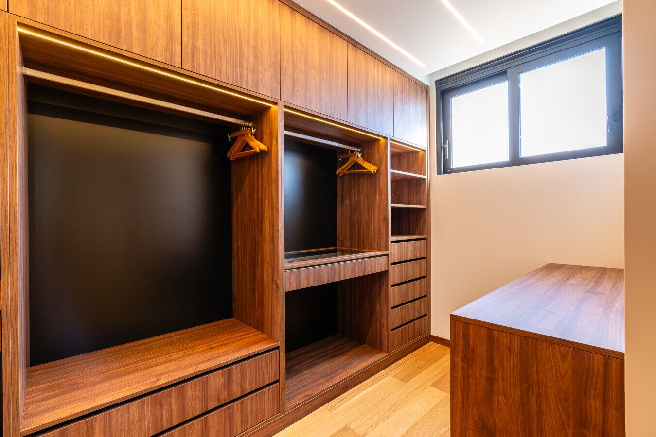 Ein begehbarer Kleiderschrank mit Holzausstattung, mehreren Regalen und Kleiderstangen.