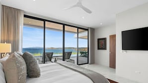 Ein modernes Schlafzimmer mit einem großen Bett, Meerblick und einem Balkon mit Sitzgelegenheit.