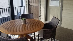 Un balcon avec une table ronde en bois, des chaises en osier et un tapis à motifs.