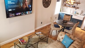 Un salon doté d’un grand téléviseur à écran plat fixé au mur, d’un canapé en cuir marron avec des coussins bleus, d’une table basse et d’un coin repas avec une petite table et des chaises.