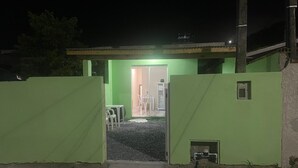Un edificio con fachada verde, entrada visible y un pequeño espacio al aire libre con sillas.