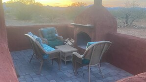 Un espace extérieur aménagé avec des chaises en osier et un sol en briques, offrant une vue sur un paysage désertique.