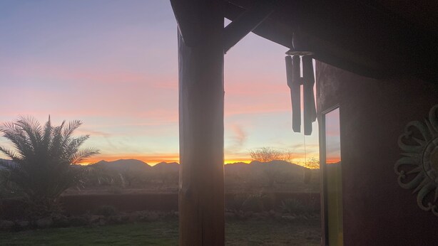 Une vue sur le coucher de soleil depuis un espace extérieur abrité, doté d’une structure en bois et d’un mur décoratif.