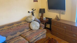 Un salon avec un canapé à motifs, un téléviseur fixé au mur, une lampe et un climatiseur mural.