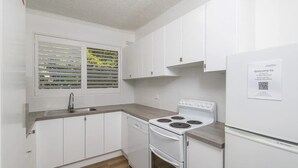 Een moderne keuken met witte kasten, een roestvrijstalen spoelbak, een inbouwvaatwasser, een wit fornuis en een koelkast.