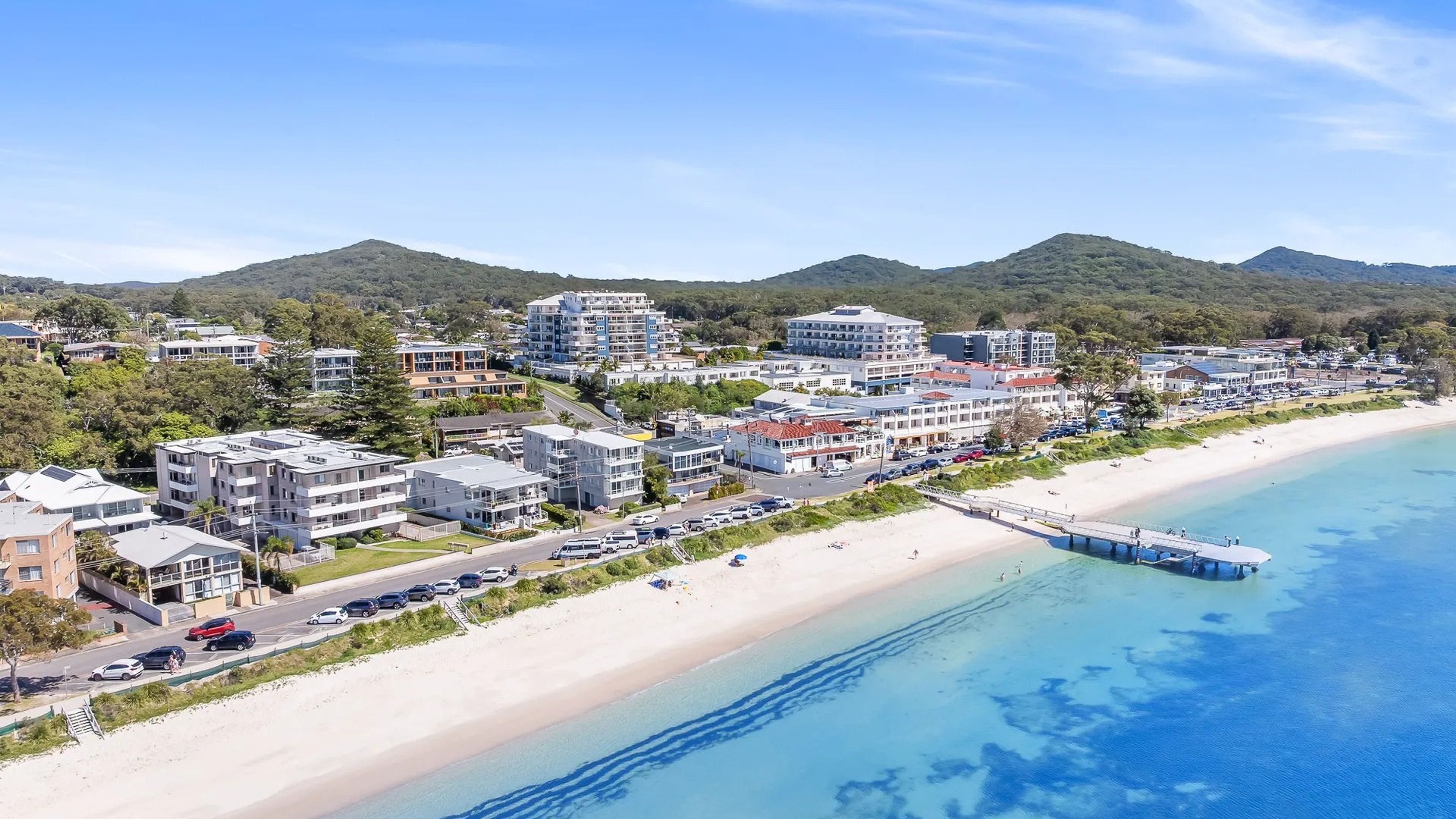 A coastal town with beachfront properties, a pier, and a mountain backdrop.