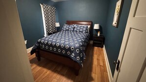 A bedroom with a bed, two bedside tables, a window with a patterned curtain, and a door. - Withrow Retreat (Waterville)
