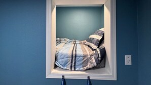 A bed in a window alcove with a blue wall, a white frame, and a striped blanket. - Withrow Retreat (Waterville)