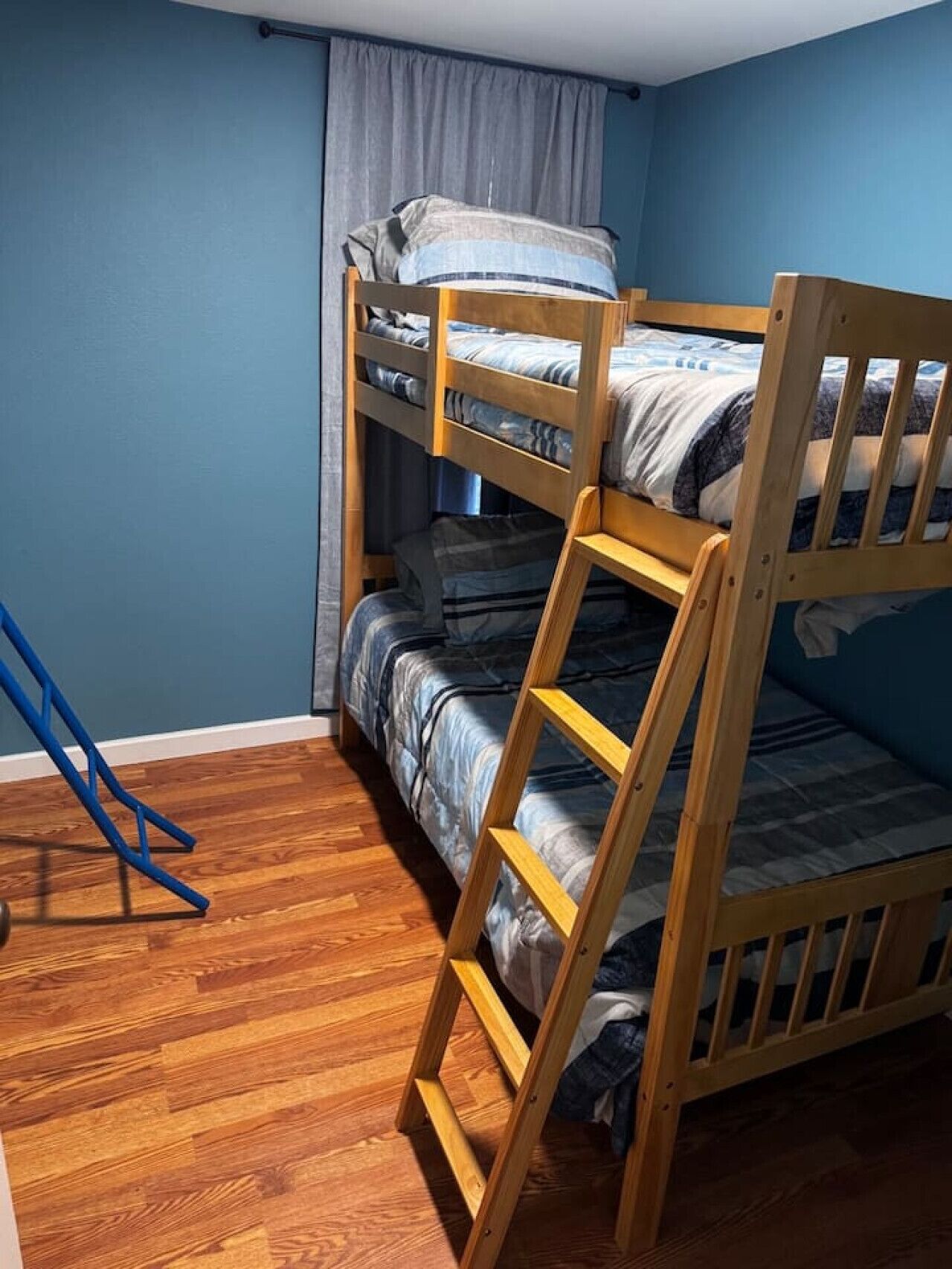 A bunk bed room with a wooden ladder, a blue wall, and a wooden floor.