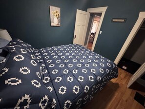 A bedroom with a patterned bedspread, a door, and a wall-mounted picture.