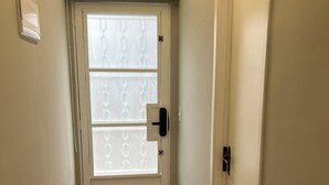 Un pasillo con piso de madera, una puerta blanca con panel de vidrio esmerilado y una unidad de aire acondicionado instalada en el techo.