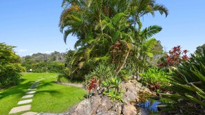Un jardín con terraza de madera, un pequeño estanque y diversas plantas tropicales.