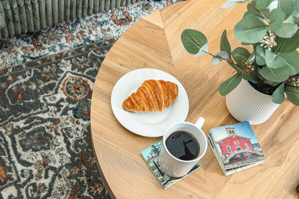 Une table ronde en bois, sur laquelle se trouvent un croissant sur une assiette blanche, une tasse de café et des cartes postales.