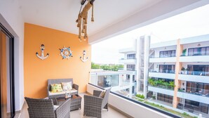 Un balcón con mobiliario de mimbre, vistas de edificios cercanos y anclajes decorativos en la pared.