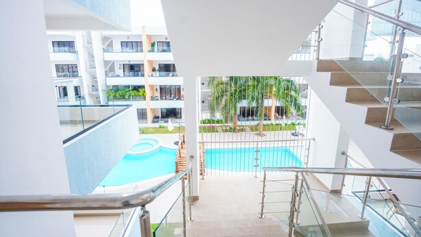 Interior moderno de un hotel con una escalera de cristal que da a un área de piscina rodeada de follaje.