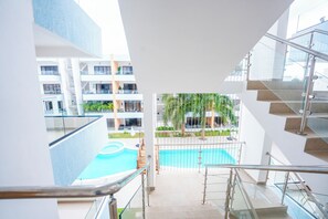 Un intérieur d’hôtel moderne avec un escalier en verre menant à un espace piscine entouré de verdure.