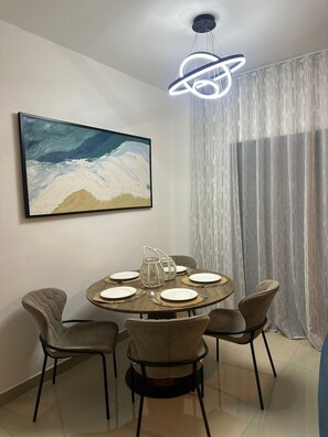 Un coin repas avec une table ronde dressée pour quatre personnes, entourée de chaises rembourrées. Un grand tableau abstrait est accroché au mur au-dessus de la table.