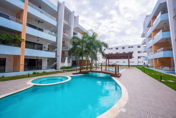 Un immeuble d’appartements moderne doté d’une piscine, de balcons et d’un petit pont.