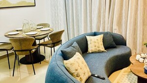Una sala de estar moderna con un sofá azul curvo, una mesa de comedor con sillas y un cuadro abstracto grande en la pared.