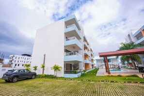 Un immeuble moderne à plusieurs étages, doté d’une piscine, d’un espace extérieur couvert et d’un parking.
