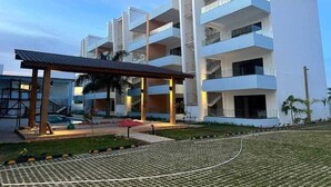 Un hotel de varios pisos con un diseño moderno, que cuenta con balcones en cada planta, un área exterior techada y una piscina.