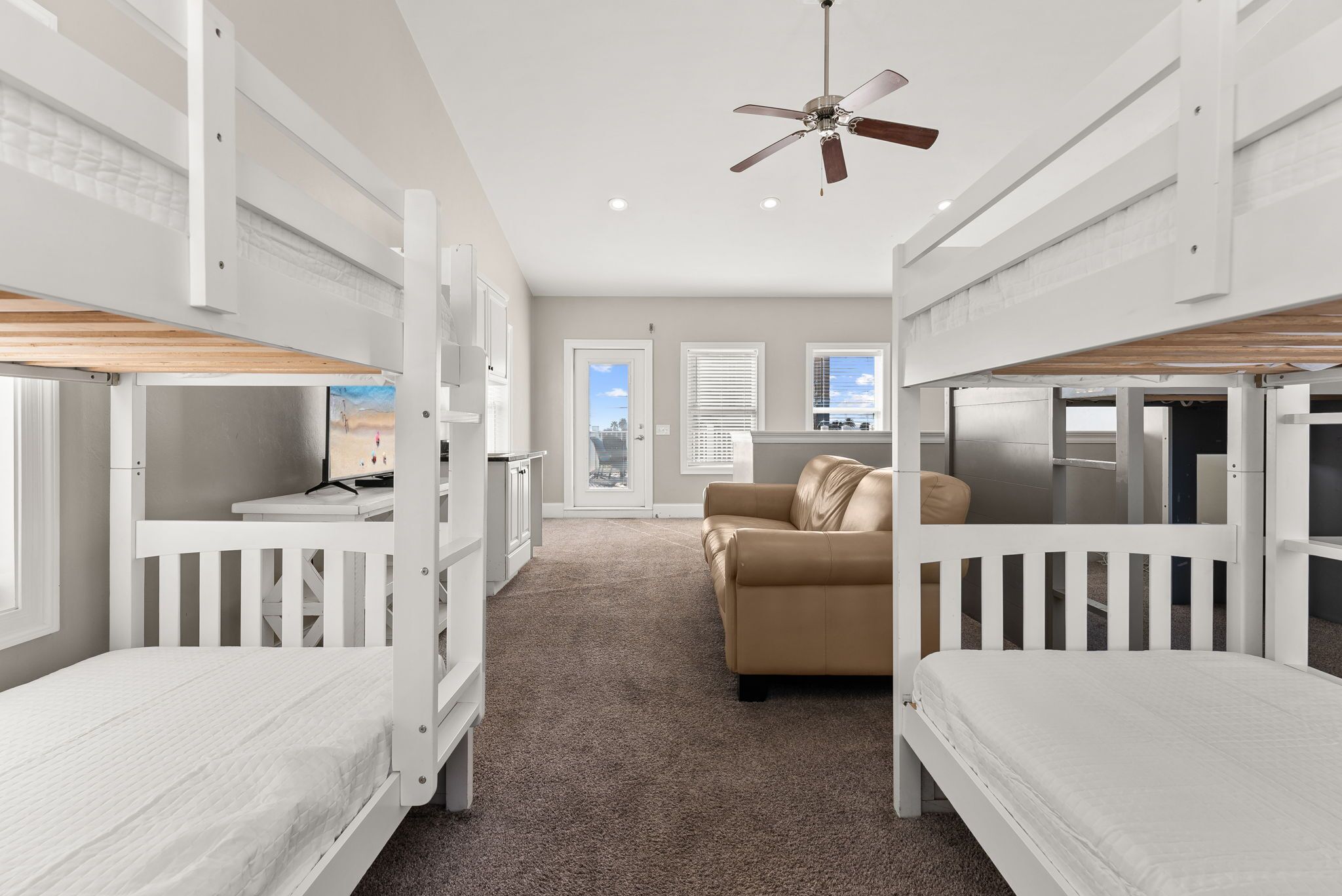 A room with bunk beds, a desk, a chair, a sofa, and a ceiling fan.
