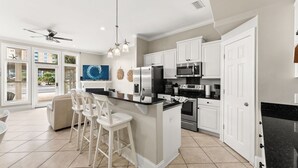 A modern kitchen with a central island, white cabinetry, stainless steel appliances, and a large window with blinds. - Gulf Views - Private Pool - 4 Bedroom (Panama City)