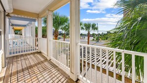 A covered porch with a wooden floor and white railings, overlooking a street with palm trees and a clear sky. - Gulf Views - Private Pool - 4 Bedroom (Panama City)