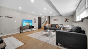 Una sala moderna con un sofá gris, una mesa de centro y un televisor. Una escalera conduce a un nivel superior.