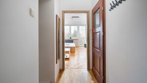 Un couloir mène à une pièce dotée d’un plancher en bois, d’un lit et d’une fenêtre.