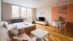 Une pièce moderne et bien éclairée, comprenant un lit, un canapé, une table à manger avec des chaises, un téléviseur et des œuvres d’art accrochées aux murs.