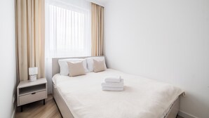 Een keurig opgemaakt hotelkamer met een bed, kussens, een nachtkastje en een raam met gordijnen.