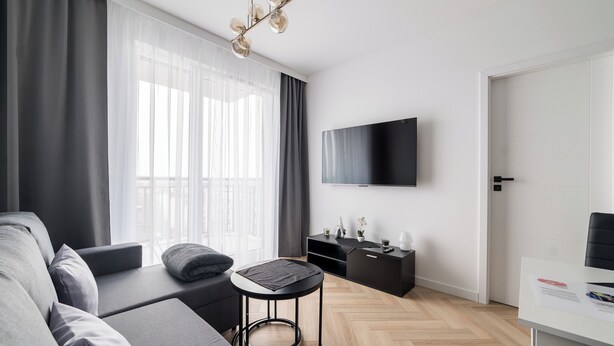 Een moderne woonkamer met een bank, een ronde tafel, een flatscreen televisie aan de muur en een houten visgraatvloer.