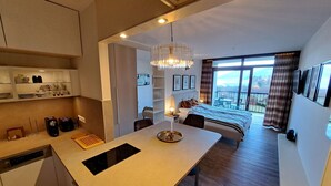 A modern hotel room with a kitchen area, a dining table, a large bed, and a balcony with a view. - Studio Landskron Seezugang by Interhome (Ossiacher See)