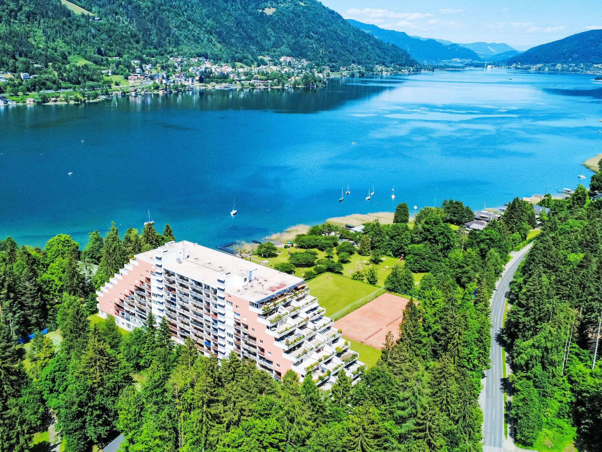 A high-rise hotel with multiple floors, surrounded by lush greenery and a lake.