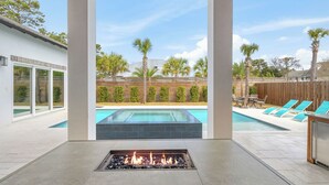 Uma área externa moderna para relaxar, com lareira, piscina e espreguiçadeiras.